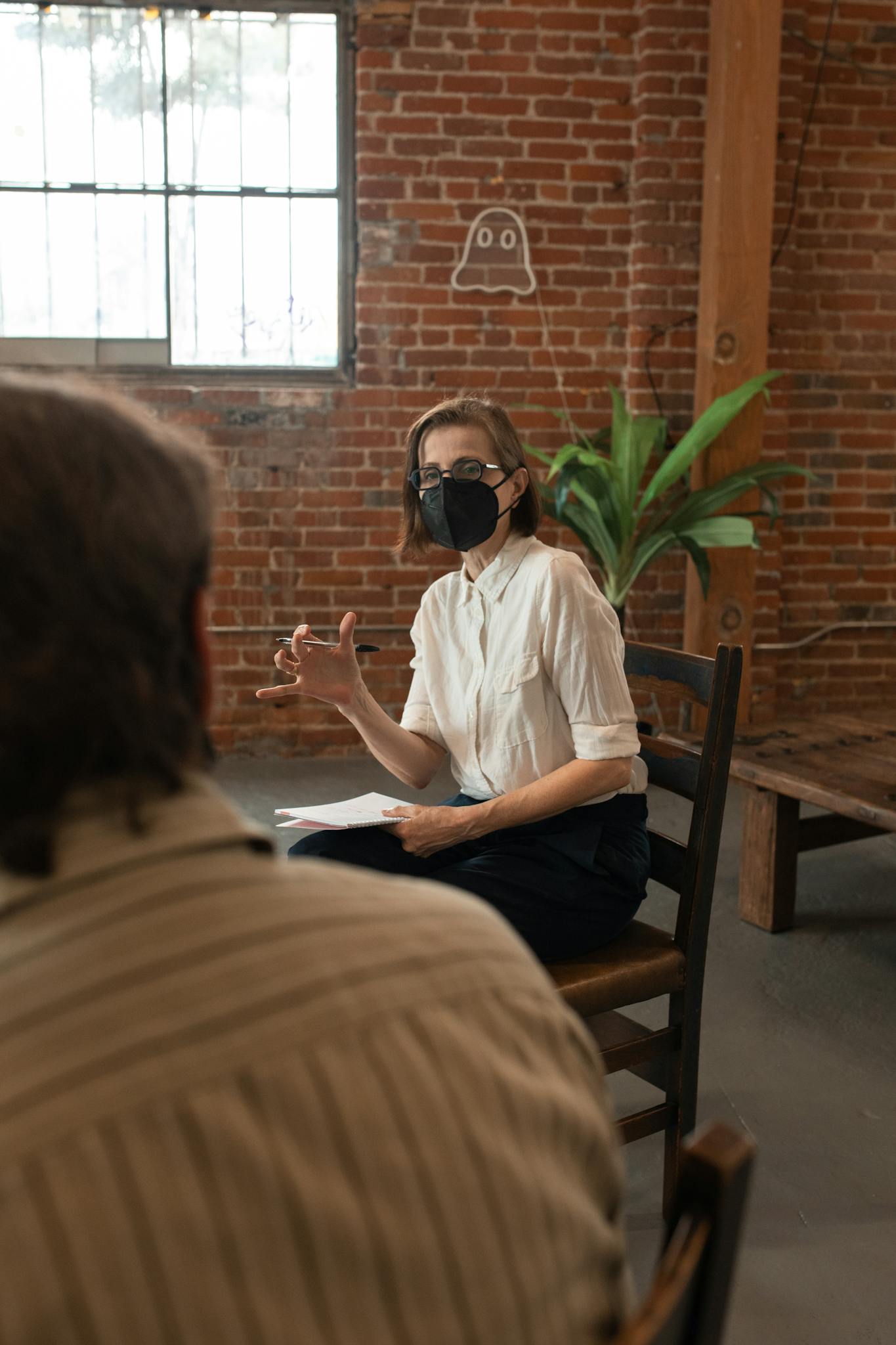 Woman in mask discussing in a casual indoor setting with a small group.